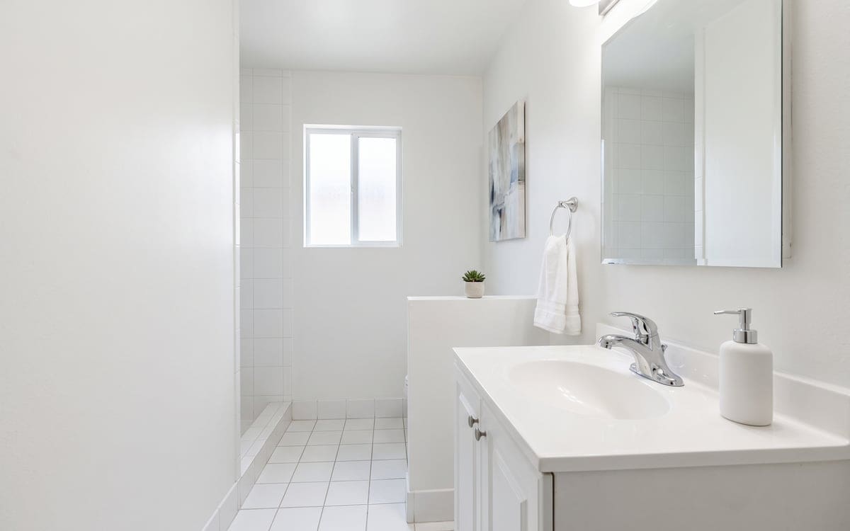 A white guest bathroom after a one time cleaning service, with a dry vanity, chrome faucet, soap pump and a towel on the ring.