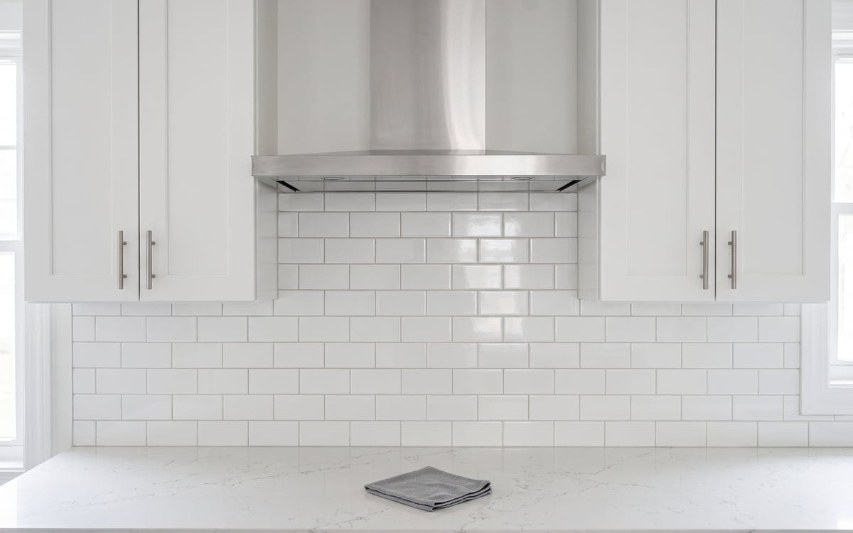 Part of what a deep cleaning includes: a stainless range hood and white subway tile backsplash, with a folded gray cloth on the quartz counter.